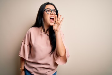 Young brunette elegant woman wearing glasses over isolated background shouting and screaming loud to side with hand on mouth. Communication concept.