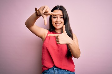 Obraz na płótnie Canvas Young brunette woman wearing casual summer shirt over pink isolated background smiling making frame with hands and fingers with happy face. Creativity and photography concept.