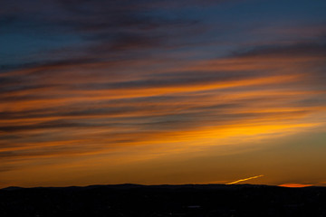 Romantic yellow-orange sunset, trace of an airplane in the sky, dark silhouette of the city. Colorful sky and plane trail over the city