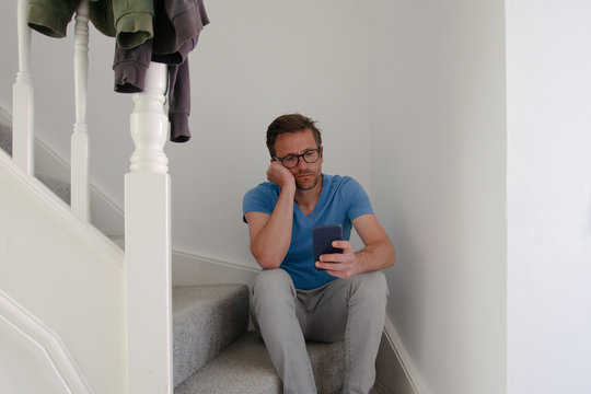 Man sitting on stairs using phone, looking sad