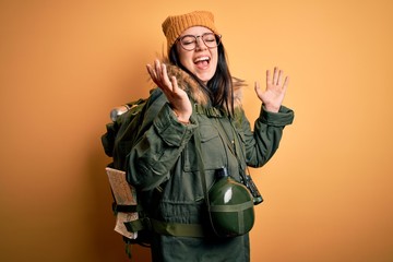 Young hiker woman wearing hiking backpack, canteen and map over yellow background celebrating mad and crazy for success with arms raised and closed eyes screaming excited. Winner concept