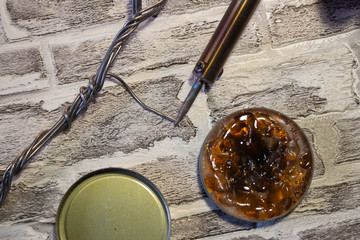 Soldering iron with a blue handle, rosin and soldering tin on a brick wall background.