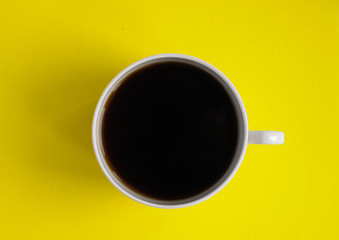 white mug with coffee on an isolated yellow background top view