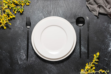 White plates and black cutlery set on black rustic background. Table setting.