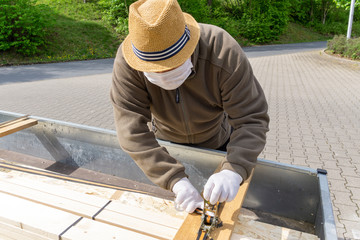 older man secures the load on his car trailer, wears a breathing mask for protection