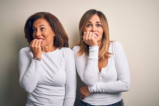 Middle age beautiful couple of sisters wearing casual t-shirt over isolated white background looking stressed and nervous with hands on mouth biting nails. Anxiety problem.