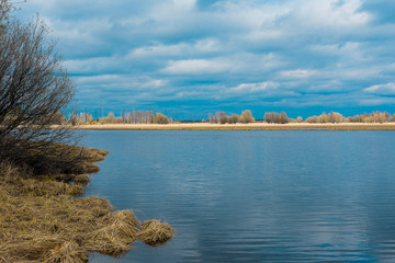 Bank with yellow grass and reflected blue sky in the river water. High contrast of blue and orange.