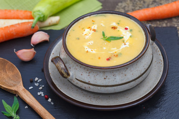 Fresh carrot soup with ingredients on black board. Homemade healthy vegetable soup in a bowl.