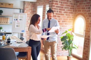 Obraz premium Two middle age business workers smiling happy and confident. Standing with smile on face working together holding documents at the office