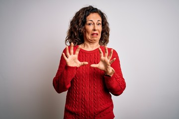 Middle age brunette woman wearing casual sweater standing over isolated white background afraid and terrified with fear expression stop gesture with hands, shouting in shock. Panic concept.
