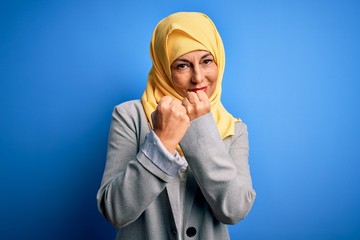 Middle age brunette business woman wearing muslim traditional hijab over blue background Ready to fight with fist defense gesture, angry and upset face, afraid of problem