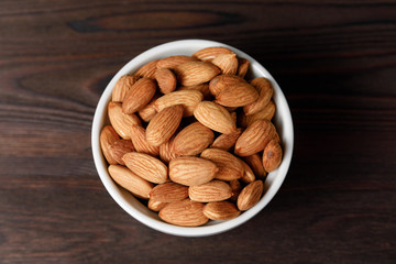 Almonds in white porcelain bowl on wooden table.