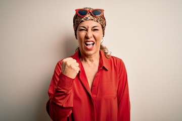 Middle age brunette woman wearing handkerchief on head and shirt over white background angry and mad raising fist frustrated and furious while shouting with anger. Rage and aggressive concept.