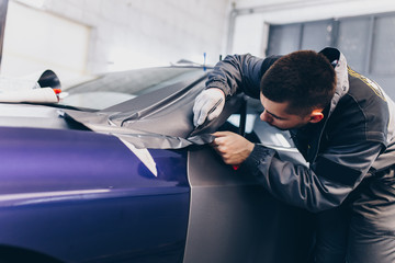 Car wrapping specialist putting vinyl foil or film on car. Selective focus. 