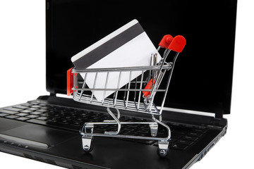 A credit card in a miniature shopping cart on a laptop. E-commerce and online shopping concept.