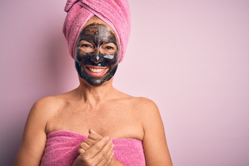 Middle age brunette woman wearing beauty black face mask over isolated pink background with hands together and crossed fingers smiling relaxed and cheerful. Success and optimistic