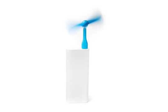 A portable blue usb fan is spinning powered by a silver power bank isolated on a white background.