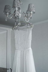 the bride's wedding dress hangs on the chandelier. wedding. selective focus. film grain.