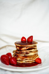 Close-up delicious pancakes, with strawberries and syrup on a light background. Sweet syrup flows from a stack of pancake