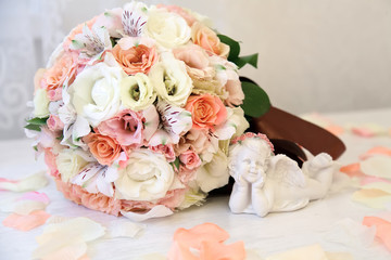 The bride's bouquet is on the table of pink flowers. the figure of an angel lies next to a bouquet of rose petals on the table.