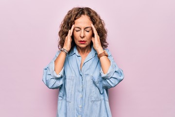 Middle age beautiful woman wearing casual denim shirt standing over pink background with hand on headache because stress. Suffering migraine.