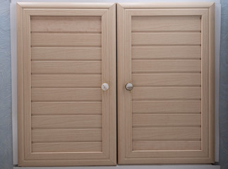 Two doors made of beige wooden boards with round handles. Homemade window shutters.