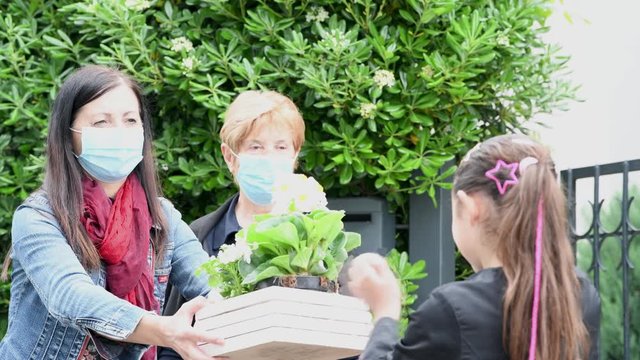 Young girl handing a plant to two women wearing masks for coronavirus emergency