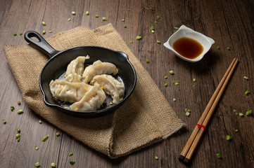 Gyozas, fried japanese dumplings on cast-iron pan served with soy sauce. wooden texture background.