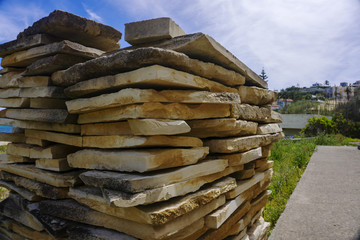 Close up of pile of natural flat stones for construction, against bright blue sky. Construction store stack on green grass.