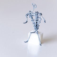 A man of wire sits on a piece of sugar, spreading his hands, symbolizing insecurity, frustration