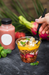 Yoghurt with granola and fruit in a plastic glass on a black background. Freshly smoothie. Food delivery. Healthy food