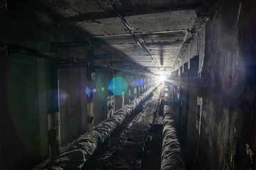 Underground concrete utility tunnel with pipes and wires. Utility tunnel with light in the end.