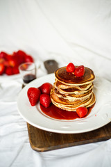 Close-up delicious pancakes, with strawberries and syrup on a light background. Sweet syrup flows from a stack of pancake