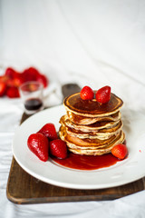 Close-up delicious pancakes, with strawberries and syrup on a light background. Sweet syrup flows from a stack of pancake