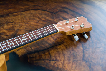 Close-up of a ukulele fretboard - small light brown instrument on beautiful wooden table.