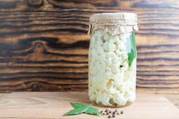 Fermented vegetables cauliflower, in glass jar on wood background.