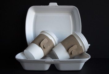 Two used disposable cups in a plastic food container close-up on a black background and space for...