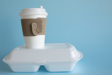 Fototapeta na wymiar A disposable coffee Cup and a white container with food close-up on a blue background and space for copying. The concept of food delivery takeaway