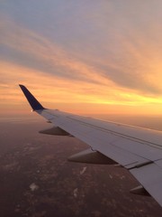 Naklejka na ściany i meble Cropped Image Of Airplane Flying Over Landscape Against Sky At Sunset
