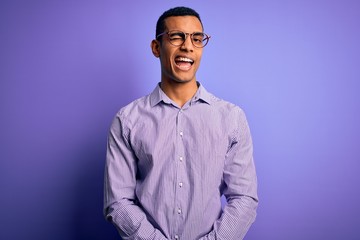 Obraz premium Handsome african american man wearing striped shirt and glasses over purple background winking looking at the camera with sexy expression, cheerful and happy face.