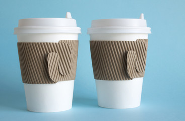 Two white disposable coffee cups close up on a blue background and a copy space