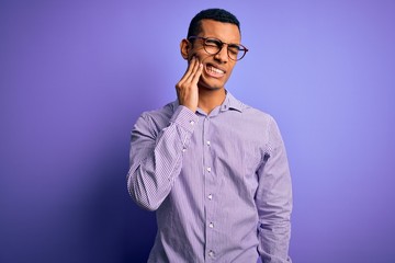 Handsome african american man wearing striped shirt and glasses over purple background touching mouth with hand with painful expression because of toothache or dental illness on teeth. Dentist