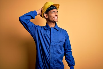 Young handsome african american worker man wearing blue uniform and security helmet smiling confident touching hair with hand up gesture, posing attractive and fashionable