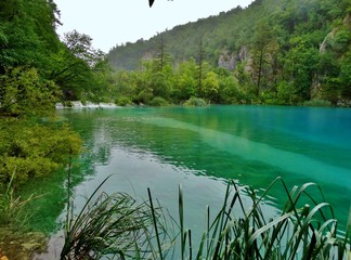 Imagen primaveral de pasarelas flotantes de madera junto a cascadas y lagos azules con antiguos...