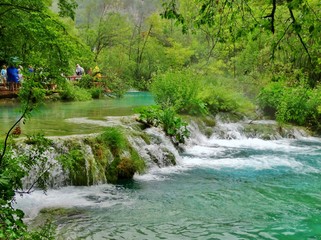 Imagen primaveral de pasarelas flotantes de madera junto a cascadas y lagos azules con antiguos...