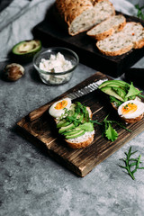 Whole grain bread sandwich with avocado, arugula, egg and cream cheese on a table