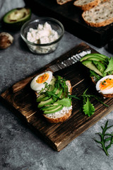 Whole grain bread sandwich with avocado, arugula, egg and cream cheese on a table