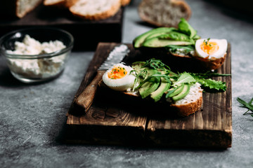 Whole grain bread sandwich with avocado, arugula, egg and cream cheese on a table