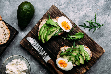 Whole grain bread sandwich with avocado, arugula, egg and cream cheese on a table