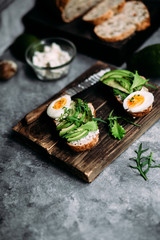 Whole grain bread sandwich with avocado, arugula, egg and cream cheese on a table